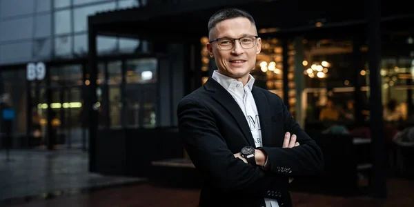 Марк Марченко, СЕО SENSAR Development, стоїть з руками схрещеними біля сучасної будівлі