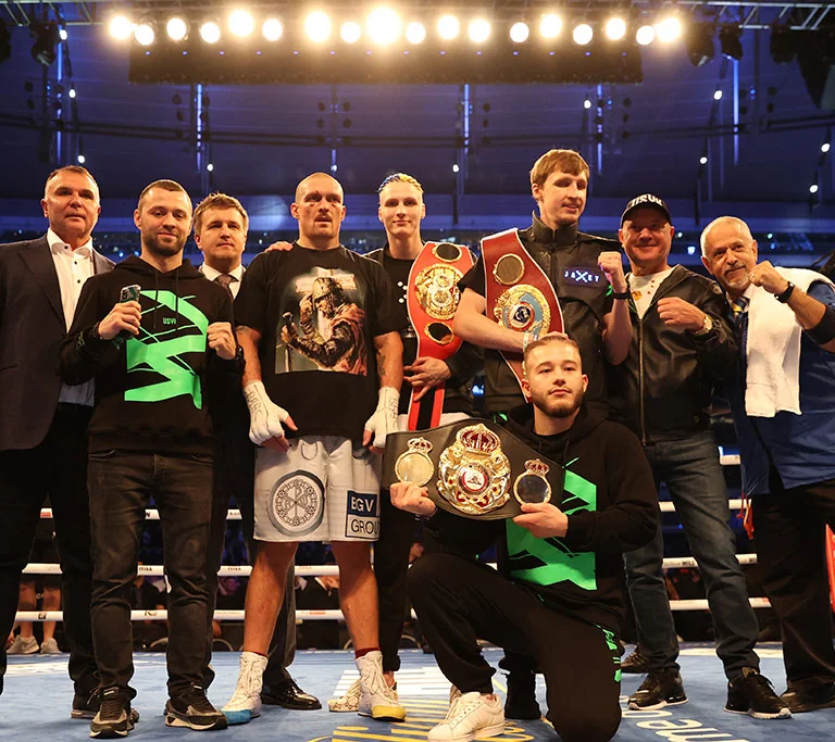 Олександр Усик з командою тримає пояси WBA, WBC та IBF на боксерському рингу
