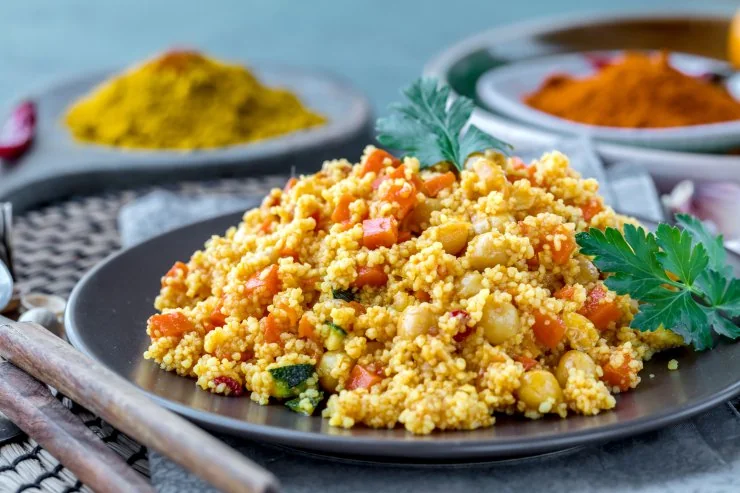 Кускус с овочами, куркумой, паприкой и зеленью на тарелке