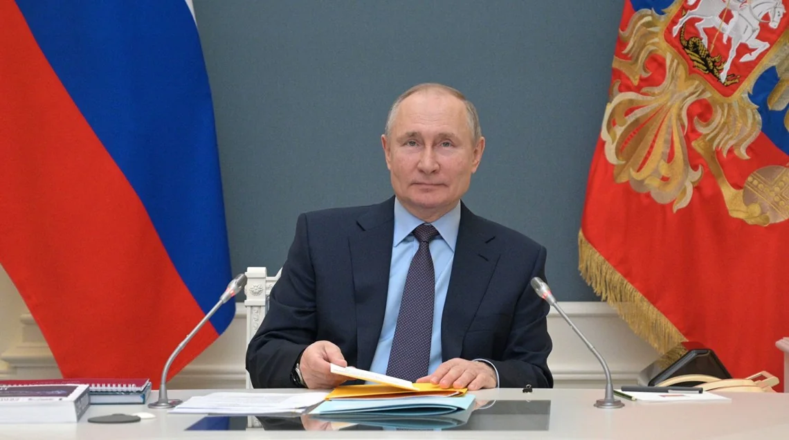 Володимир Путін за столом з документами на тлі прапорів Росії