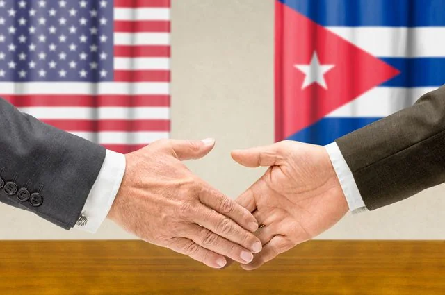 Дипломатичне рукостискання представників США та Куби на тлі прапорів