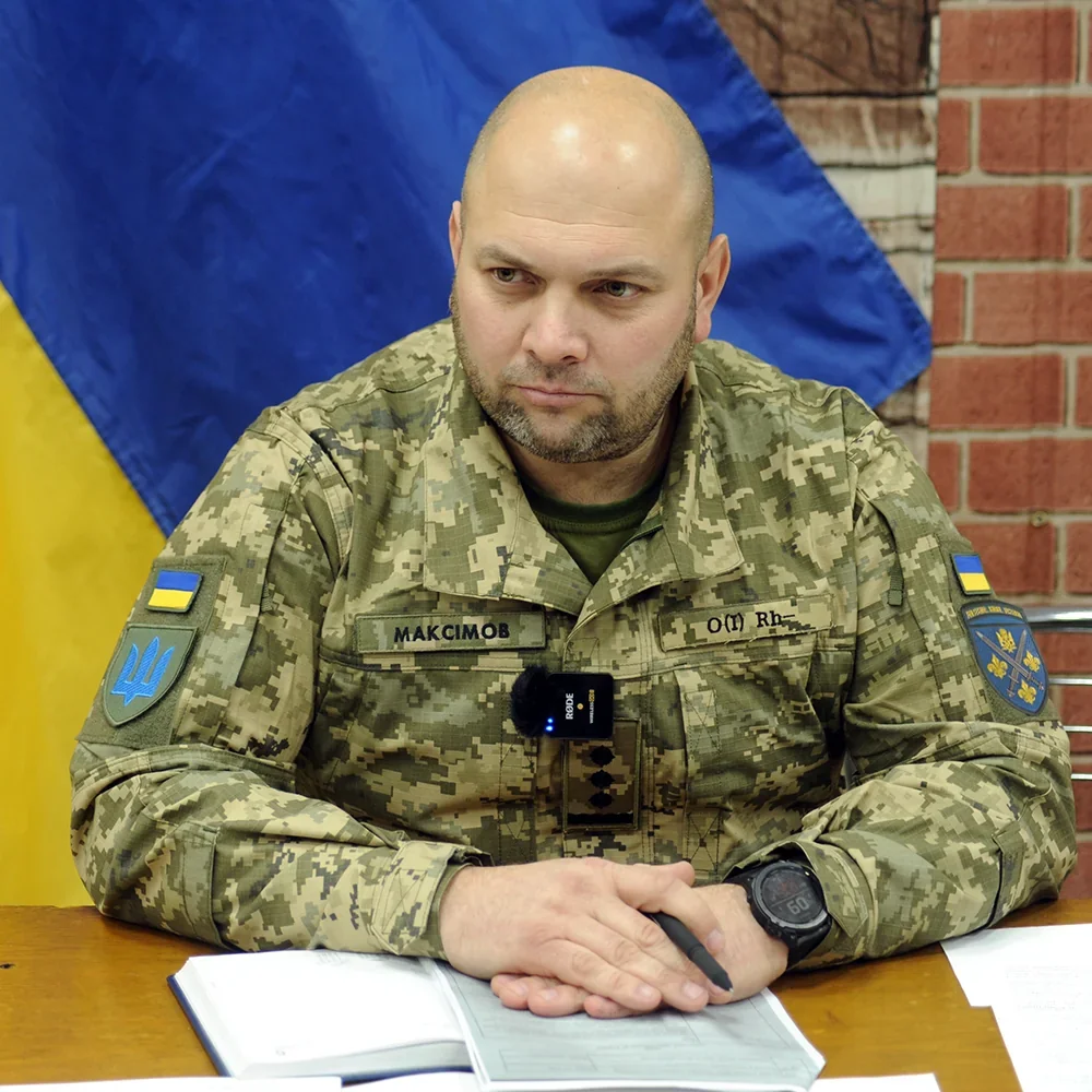 Офіцер ЗСУ Максимов у камуфляжі за столом з документами на фоні прапора