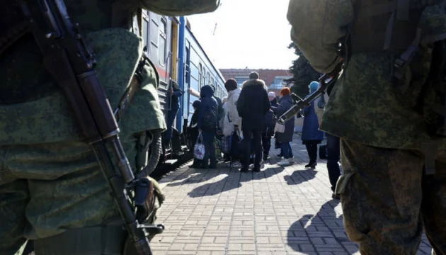 Озброєні військові етапують українських вязнів до потяга для вивезення до РФ