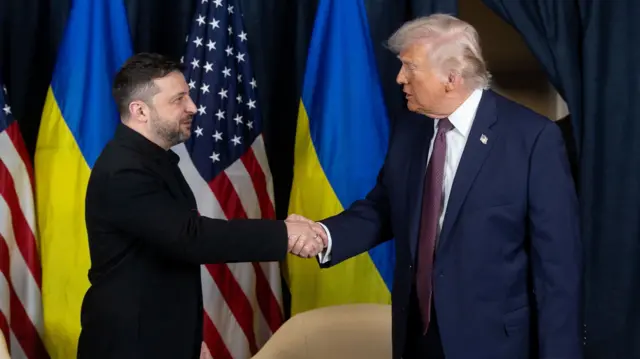 Дональд Трамп і Володимир Зеленський тиснуть руки на тлі прапорів США та України
