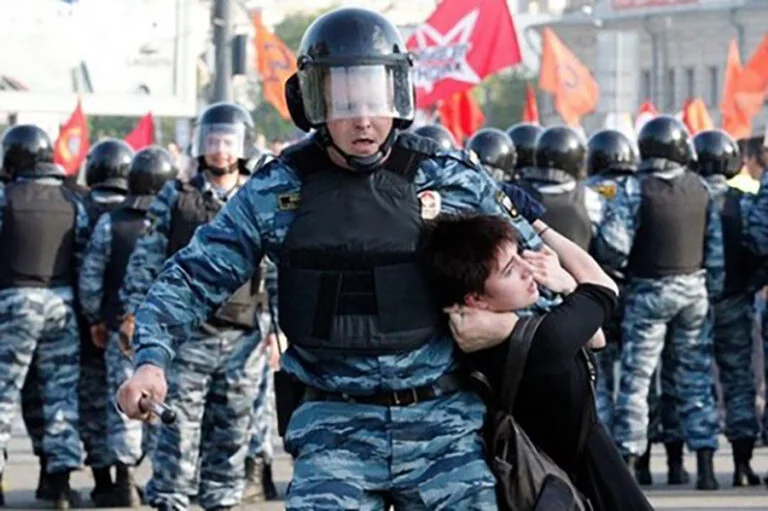 Російські силовики затримують протестувальника на тлі червоних прапорів